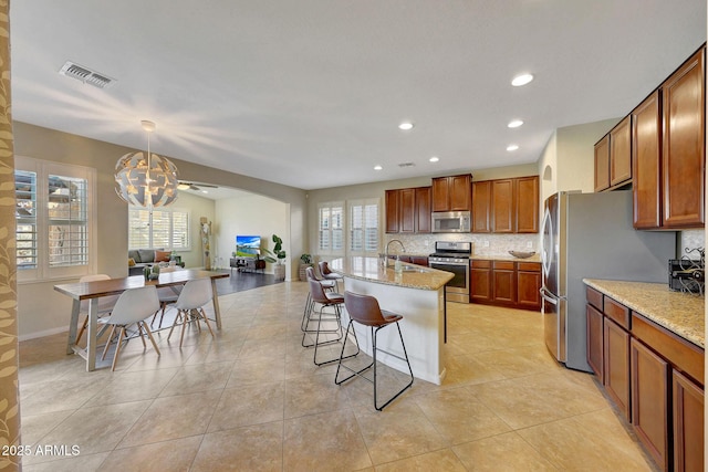 kitchen with a kitchen bar, sink, light stone counters, decorative light fixtures, and stainless steel appliances