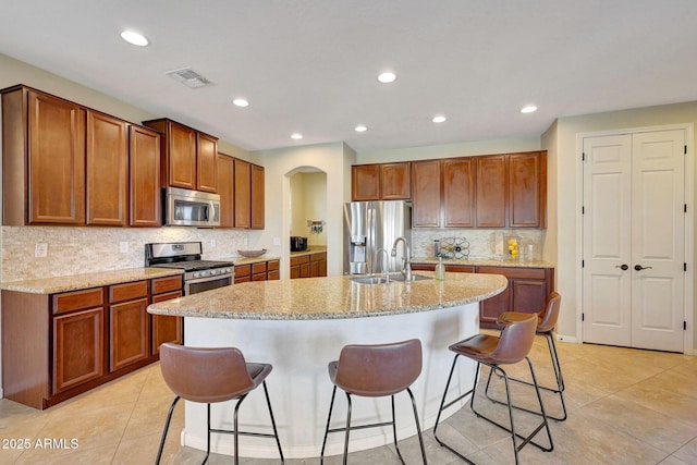 kitchen with a breakfast bar, sink, appliances with stainless steel finishes, light stone countertops, and a kitchen island with sink