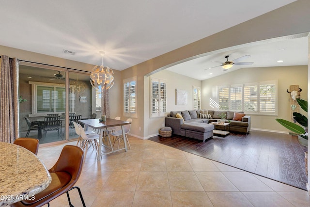 living room with ceiling fan with notable chandelier, lofted ceiling, and light tile patterned floors