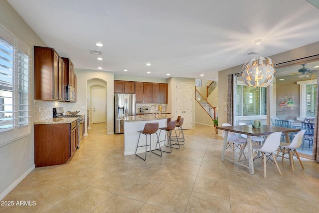 kitchen featuring pendant lighting, stainless steel appliances, an island with sink, and decorative backsplash