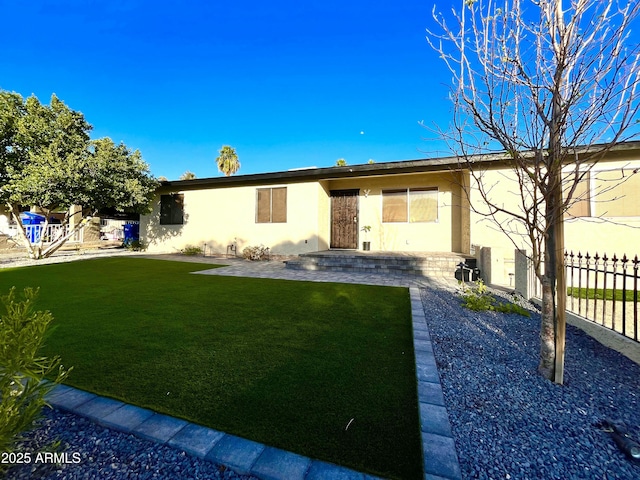 rear view of property with stucco siding, a patio, a lawn, and fence