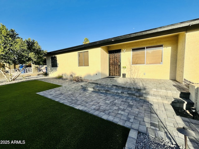 back of property with a patio area, a lawn, and stucco siding