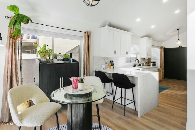 kitchen featuring white cabinetry, sink, a barn door, light hardwood / wood-style floors, and vaulted ceiling