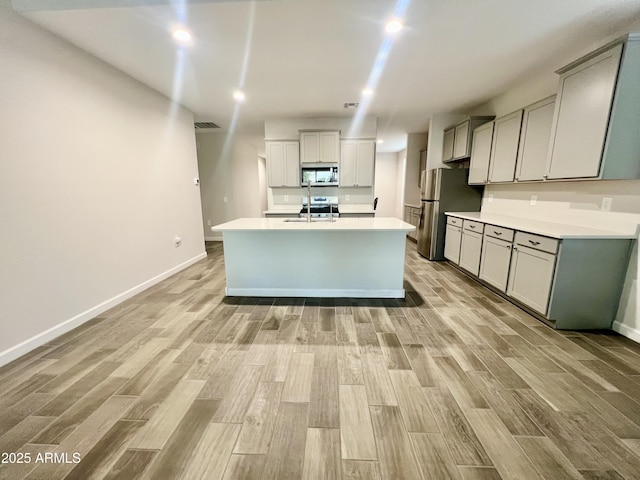 kitchen featuring a sink, light wood-style flooring, baseboards, and appliances with stainless steel finishes