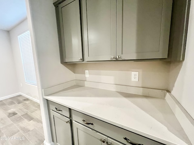 kitchen with light stone counters, gray cabinets, and baseboards