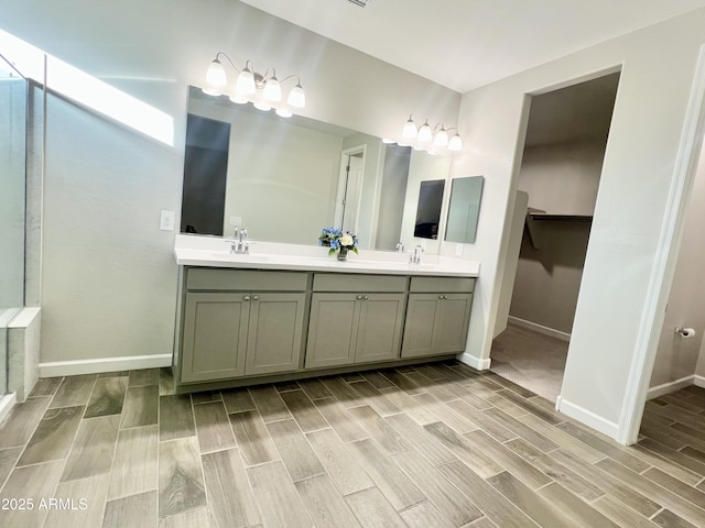 bathroom featuring wood tiled floor, baseboards, a sink, double vanity, and a spacious closet