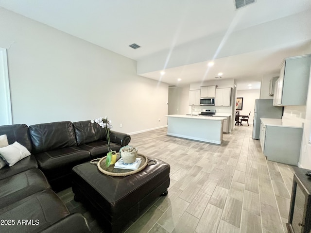 living room featuring light wood-style flooring, baseboards, visible vents, and recessed lighting