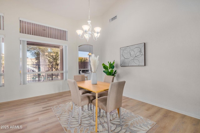 dining area with arched walkways, light wood finished floors, visible vents, and a notable chandelier