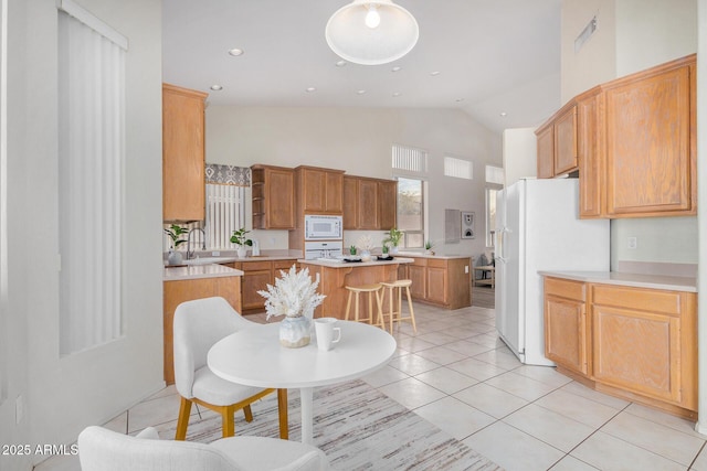 kitchen with light tile patterned floors, high vaulted ceiling, white appliances, a breakfast bar, and light countertops