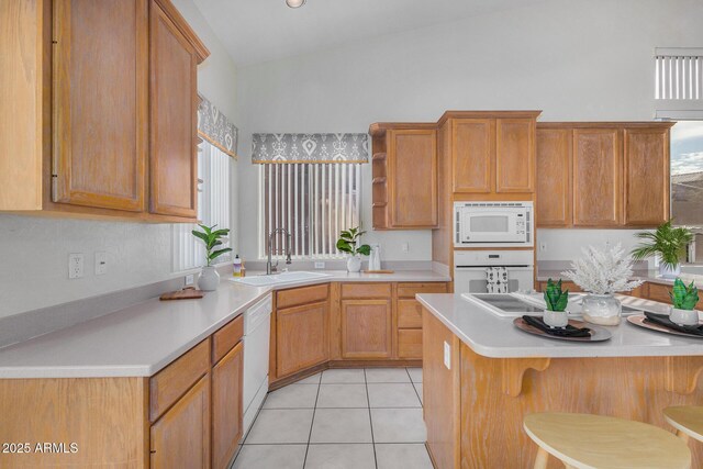 kitchen featuring vaulted ceiling, white appliances, light tile patterned floors, a kitchen island with sink, and sink