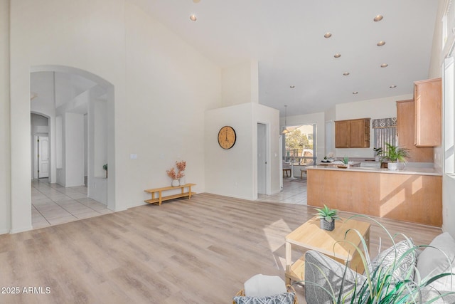 kitchen with arched walkways, light wood-style flooring, a peninsula, a high ceiling, and light countertops