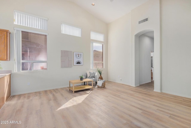 living area with arched walkways, high vaulted ceiling, light wood-style flooring, visible vents, and baseboards