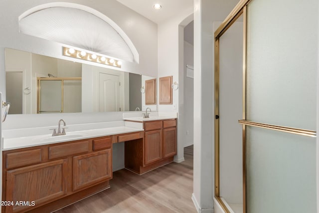 bathroom featuring double vanity, a shower stall, a sink, and wood finished floors