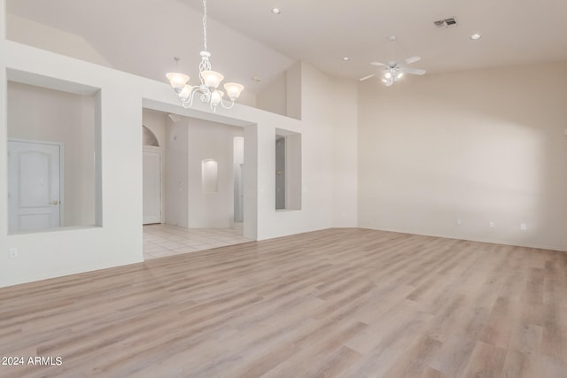 empty room with ceiling fan with notable chandelier, light hardwood / wood-style flooring, and high vaulted ceiling