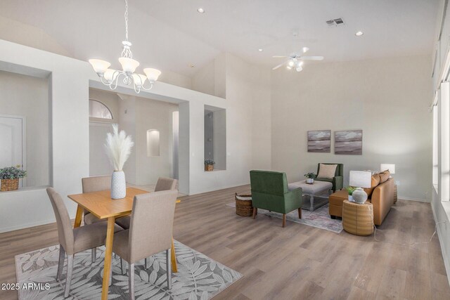 dining room featuring ceiling fan with notable chandelier, light hardwood / wood-style flooring, and high vaulted ceiling