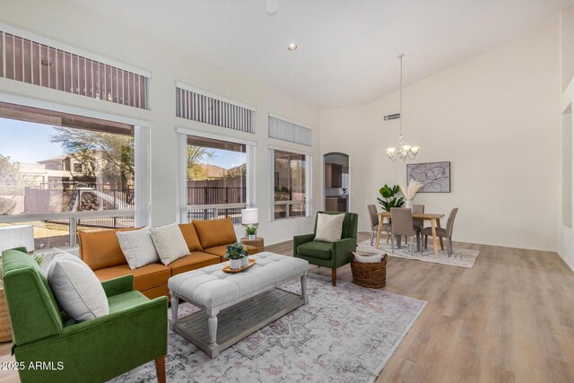 unfurnished living room with light wood-type flooring, ceiling fan with notable chandelier, and high vaulted ceiling