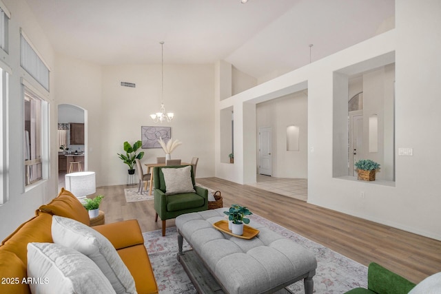 living area with light wood finished floors, visible vents, arched walkways, high vaulted ceiling, and a notable chandelier