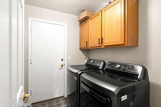 clothes washing area featuring washing machine and clothes dryer, a textured ceiling, and cabinets