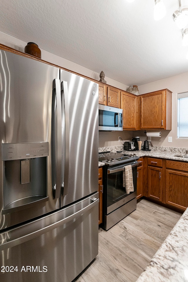 kitchen with sink, a textured ceiling, light hardwood / wood-style floors, stainless steel appliances, and light stone counters