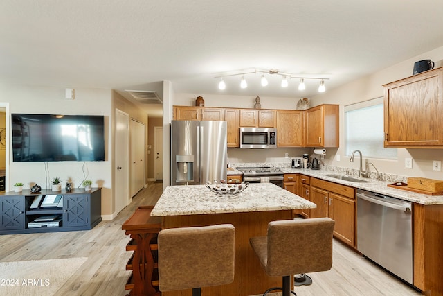 kitchen with light hardwood / wood-style flooring, stainless steel appliances, sink, a center island, and a kitchen bar