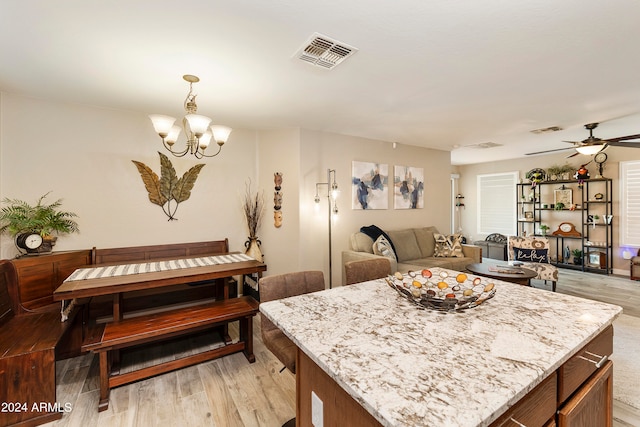 kitchen featuring a kitchen island, light stone countertops, light hardwood / wood-style flooring, ceiling fan with notable chandelier, and decorative light fixtures