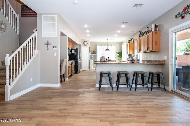 kitchen with stainless steel range oven, hanging light fixtures, light hardwood / wood-style flooring, a kitchen breakfast bar, and kitchen peninsula