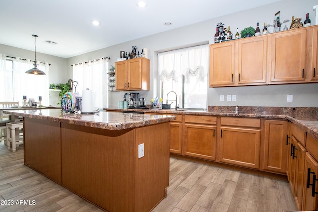 kitchen featuring decorative light fixtures, a kitchen island, dark stone counters, and light wood-type flooring