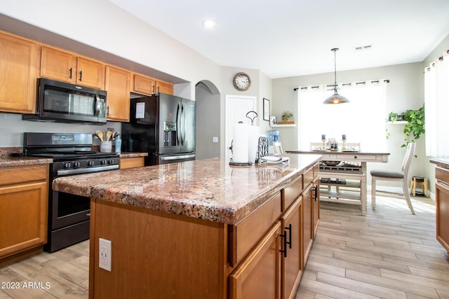 kitchen featuring black fridge with ice dispenser, stainless steel range oven, light stone counters, decorative light fixtures, and a center island