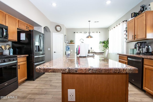 kitchen featuring hanging light fixtures, black appliances, light stone countertops, a center island with sink, and light wood-type flooring