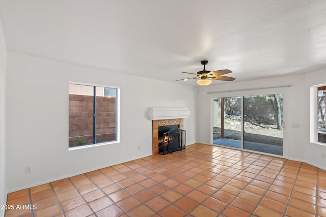 unfurnished living room with tile patterned floors, a healthy amount of sunlight, a tiled fireplace, and a ceiling fan