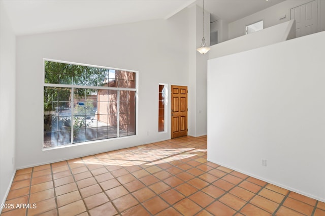 tiled empty room featuring high vaulted ceiling and baseboards
