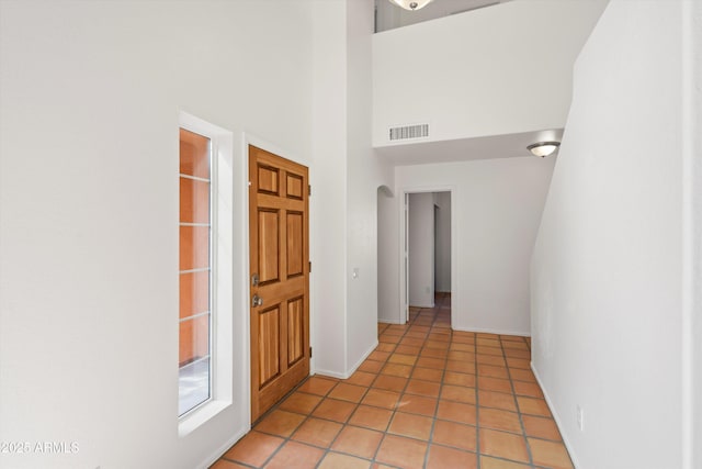 foyer entrance featuring light tile patterned floors, arched walkways, visible vents, a high ceiling, and baseboards