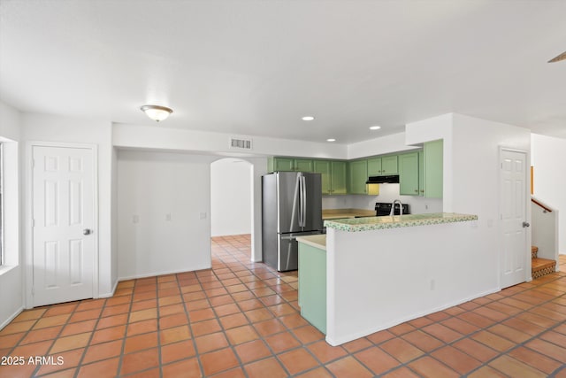 kitchen featuring visible vents, freestanding refrigerator, a peninsula, green cabinets, and tile patterned floors