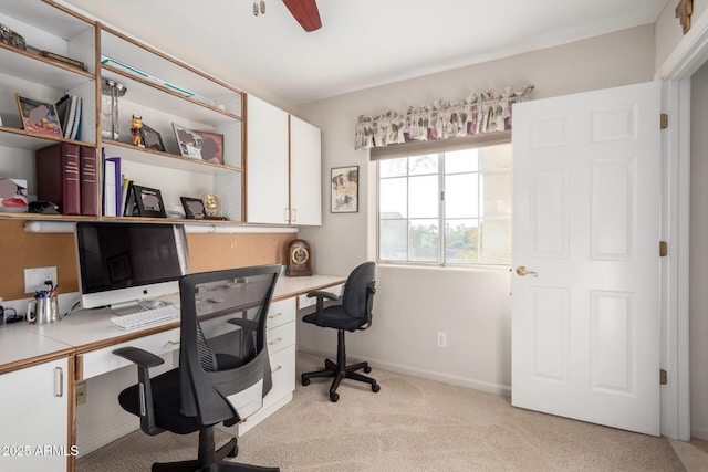 office area featuring light colored carpet, built in desk, ceiling fan, and baseboards
