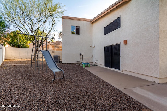 rear view of house featuring a playground, stucco siding, a fenced backyard, a tile roof, and central air condition unit