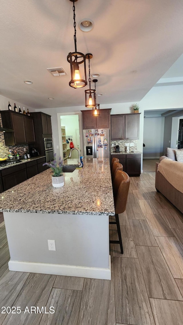 kitchen featuring decorative backsplash, appliances with stainless steel finishes, pendant lighting, and a large island with sink