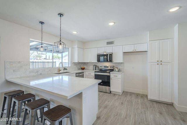 kitchen featuring white cabinets, a peninsula, a sink, and appliances with stainless steel finishes