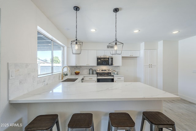 kitchen featuring a sink, decorative backsplash, stainless steel appliances, decorative light fixtures, and a peninsula