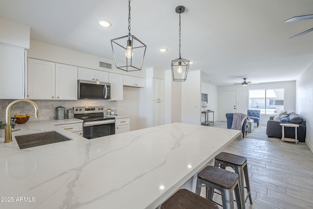 kitchen featuring a peninsula, a sink, visible vents, a ceiling fan, and appliances with stainless steel finishes