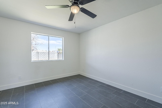empty room featuring dark tile patterned flooring, baseboards, and ceiling fan