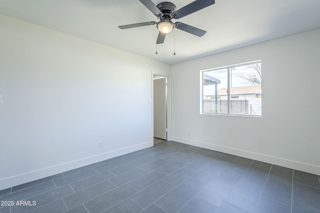 empty room with dark tile patterned floors, baseboards, and ceiling fan