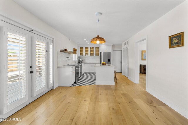 kitchen with stainless steel fridge with ice dispenser, white cabinets, light countertops, light wood finished floors, and backsplash