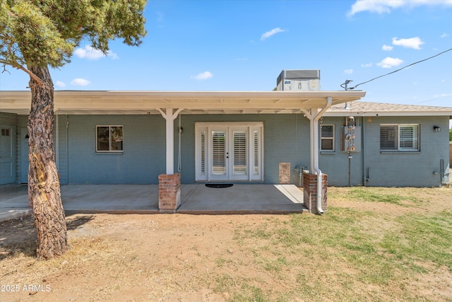 rear view of property featuring a lawn, a patio area, brick siding, french doors, and central AC unit