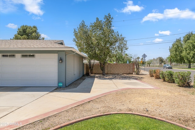 exterior space featuring a shingled roof, a garage, and fence