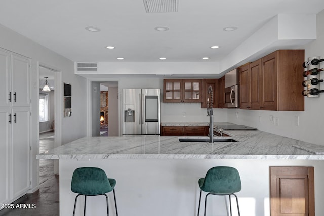 kitchen with light stone countertops, stainless steel appliances, a breakfast bar, and kitchen peninsula