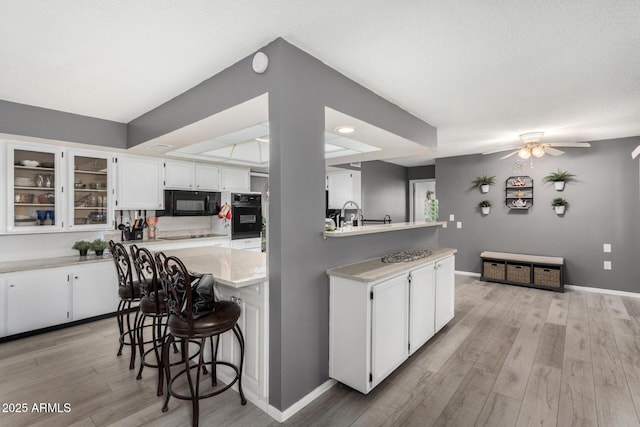 kitchen featuring white cabinetry, a breakfast bar, light hardwood / wood-style floors, and black appliances