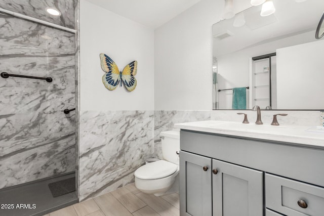 bathroom with tile walls, vanity, a shower with door, and toilet