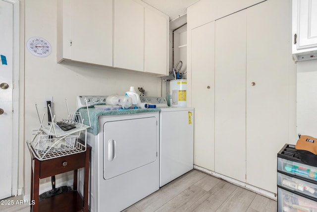 laundry area featuring water heater, washer and clothes dryer, cabinets, and light wood-type flooring