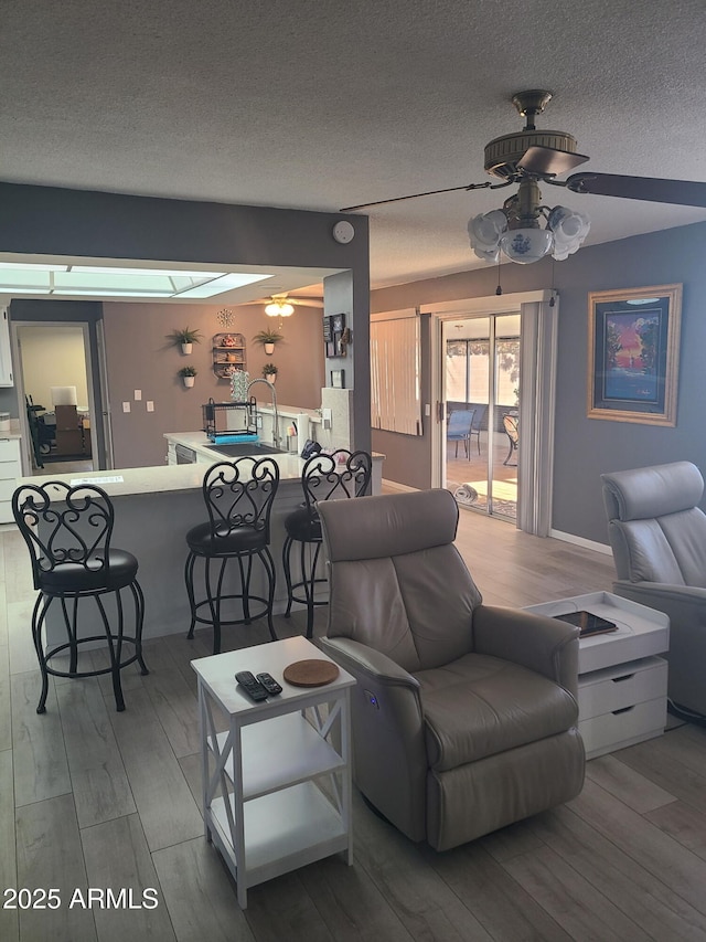 living room with ceiling fan, light hardwood / wood-style flooring, and a textured ceiling