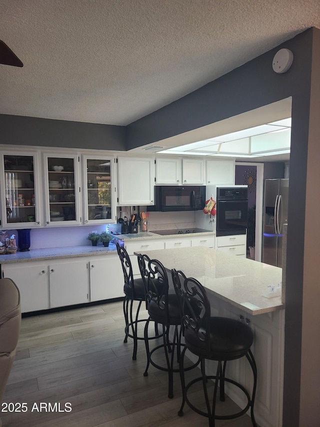 kitchen featuring white cabinetry, light stone countertops, black appliances, a textured ceiling, and light wood-type flooring